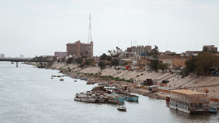Riverbank view of Baghdad with boats and city skyline during overcast weather