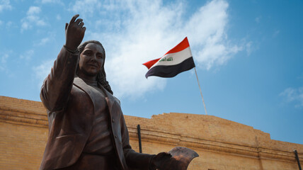 Statue of a prominent Iraqi figure with national flag waving in the background in Baghdad