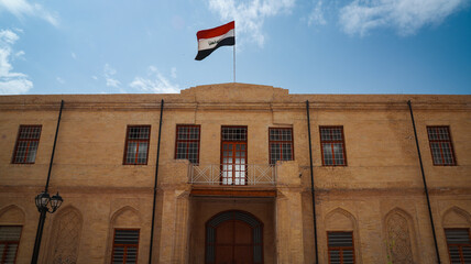 Historical building in Baghdad Iraq with national flag waving in bright sky