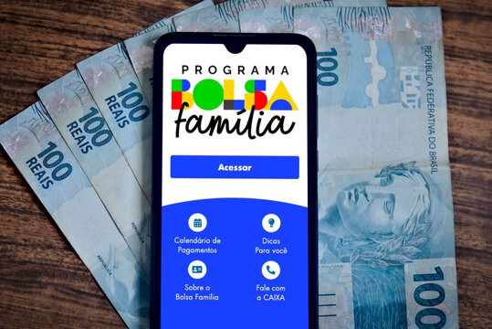 The Bolsa Fam&iacute;lia program is displayed on a smartphone screen with Reais bills in the background. The Brazilian government's Bolsa Fam&iacute;lia program helps the poorest people. 