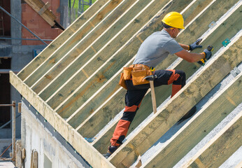 Worker Installing Roof Rafters at Construction Site Under Clear Sky in Daytime