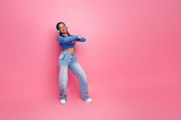 Young woman listening to music with headphones and dancing joyfully against a vibrant pink...