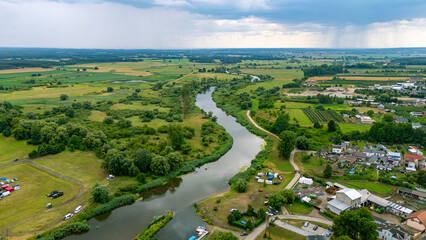 Aerial view of the town of Pyzdry in Greater Poland and the meandering Warta River. Green fields, riverside buildings, and a small marina create a picturesque rural landscape