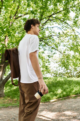 Young man enjoying a sunny day in a vibrant green park while sipping coffee