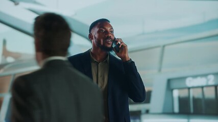A man in a suit talks on the phone near an airport gate. He seems to be waiting. - Powered by Adobe