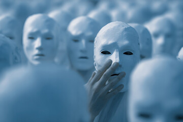 Hand touching white mask among many identical masks symbolizing anonymity identity disguise individuality concept. Copy space