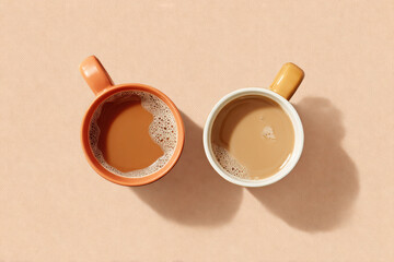 Two ceramic cups filled with coffee on beige background with foam detail creating minimalistic composition. Copy space