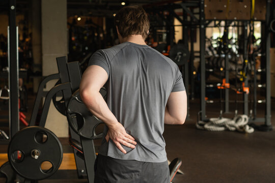 Athlete or young sporty man with pain in lower back at gym with muscle tension. Arm, inflammation or exercise with discomfort at fitness center. Close up.