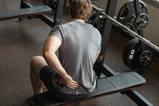 Athlete or young man sitting with pain in lower back at gym with muscle tension. Arm, inflammation or exercise with discomfort at fitness center. Close up.