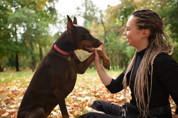 Woman Communicating with Loyal Doberman in a Sunlit Leafy Park Setting