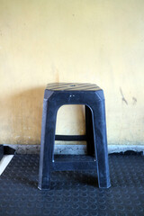 Black Plastic Stool Against Yellow Wall