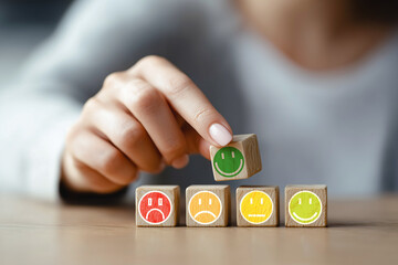 Hand choosing wooden cube with green smiley face from row of colored emoji blocks on wooden table. Studio conceptual image of customer feedback and satisfaction rating, generative ai