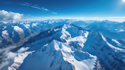 Snow-covered mountains from high altitude with clear sky and sunlight, showcasing majestic peaks and rugged terrain.
