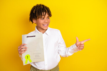 Smiling schoolboy holding first place certificate and gesturing confidently against a bright yellow background