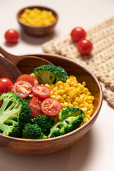 Broccoli, corn, quinoa, tomato salad in wooden bowl on light beige background. Healthy food concept