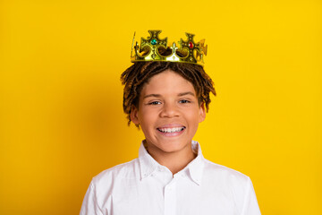 Smiling boy with gold crown stands against yellow background representing joy, confidence, and...