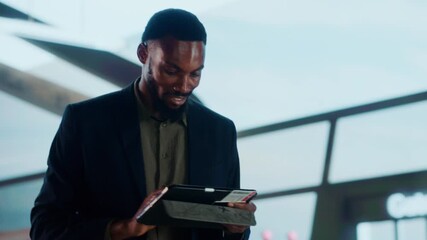 A businessman looking at a tablet in an airport. He seems happy while he is working. - Powered by Adobe