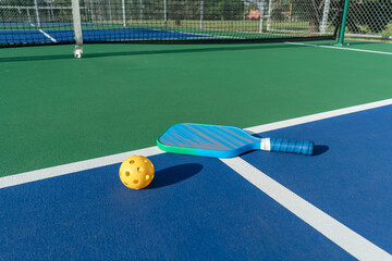 Low-angle side view of pickleball paddle and yellow ball on court surface with net