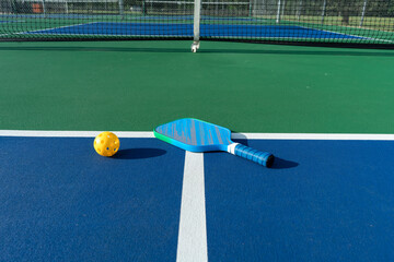 Low-angle view of pickleball paddle and ball on court surface with net