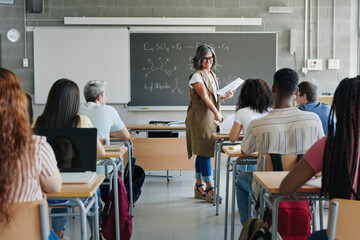 Female teacher giving exam sheet to High School students learning technology and science