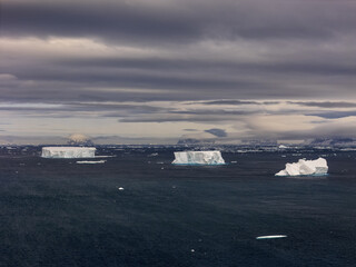 Aerial view of the stark white icebergs drift on the dark, brooding sea under a heavy, clouded sky, Seymour Island, Antarctica.