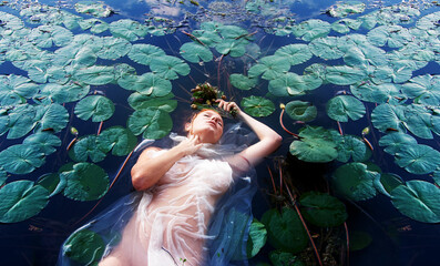 Young sexy unhappy crazy woman Lady Ophelia lies dying with rotten flowers, eyes closed in white...