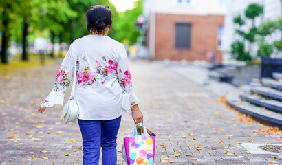 Woman walking on a tree-lined street with shopping bags during autumn afternoon