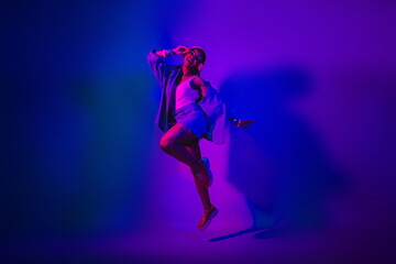 Energetic young woman dancing under vibrant neon lights in a stylish casual outfit with purple and blue hues