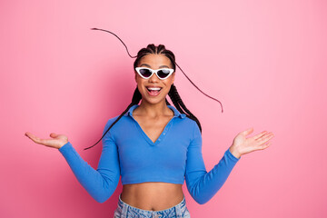 Smiling young woman with braided hair wearing white sunglass and blue top on a pink background...