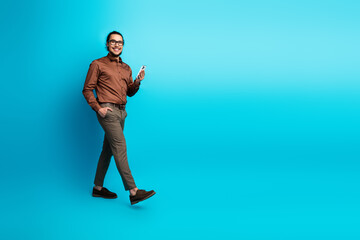 Confident young businessman holding a smartphone against a vibrant teal background showcasing...