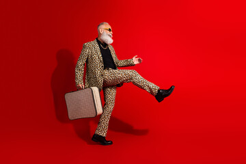 Charismatic man in leopard print suit holding suitcase and posing energetically in vibrant setting...