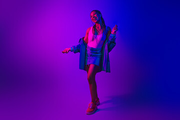 Vibrant portrait of a young woman dancing in neon lighting with stylish casual wear, exuding joyful...