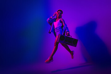Dynamic young woman with headphones and boombox dancing under neon lights in vibrant club-inspired...