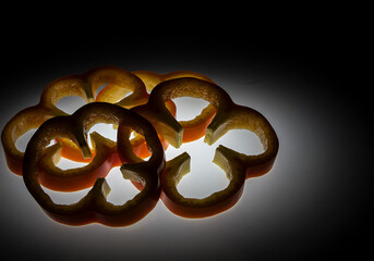 Close-up of translucent bell pepper slices, backlit against a dark background, showcasing their intricate internal structure.