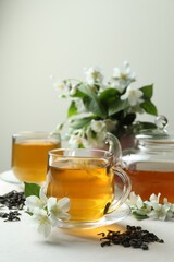 Aromatic jasmine tea in glass cups, teapot, flowers and dried leaves on white table