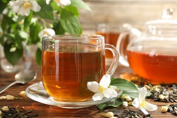 Aromatic jasmine tea in glass cup, teapot, brew and flowers on wooden table, closeup