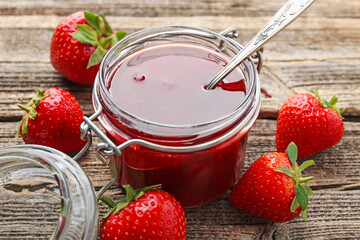 Tasty strawberry jam in glass jar and fresh berries on wooden table, closeup