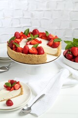 Delicious cheesecake with strawberries and mint on white wooden table