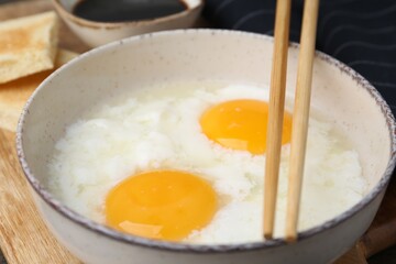 Traditional asian breakfast with half-boiled eggs in bowl, chopsticks, bread and soy sauce on table, closeup