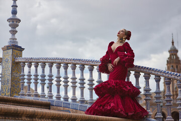 Young, beautiful, blonde woman in red flamenco dress, flowers in her hair and gold jewelry,...