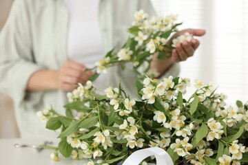 Woman making bouquet of jasmine branches at white table, closeup