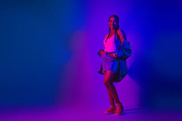 Stylish young woman posing in neon lighting wearing a denim skirt and jacket, evoking a fun night...