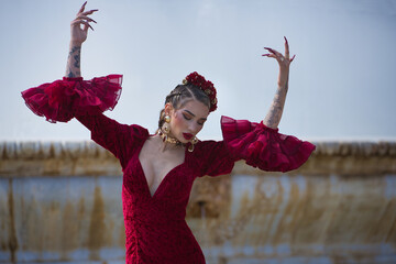 Young, beautiful, blonde woman in red flamenco dress, flowers in her hair and gold jewelry,...