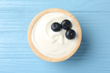 Tasty yoghurt with blueberries in bowl on light blue wooden table, top view