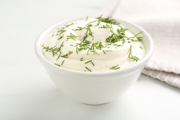 Delicious yogurt in bowl and dill on white table, closeup