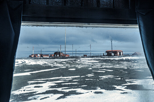 View of a research station with red buildings and antenna towers against a stark white horizon, framed by dark curtains, Seymour Island, Antarctica.