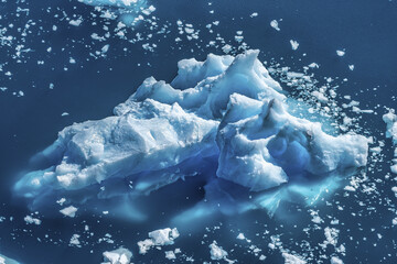 View of a jagged, luminous blue iceberg floats amidst a sea of smaller ice fragments, contrasting against the deep blue waters, Seymour Island, Antarctica.