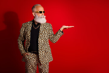 Fashionable elderly man in leopard suit making gesture on bold red backdrop showcasing eclectic...