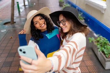 Two smiling friends taking a selfie while walking down the street