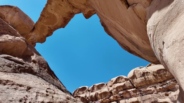 Lone tourist woman sits contemplatively under the magnificent Um Fruth rock arch in the vast expanse of Jordan's Wadi Rum desert, showcasing the stunning natural architecture